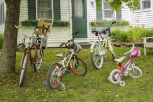 Four bicycles in front of Tyler Place accommodations. Small kid bike with training wheels, medium bike with training wheels, two adult bikes, one with a basket and one with a child seat attached