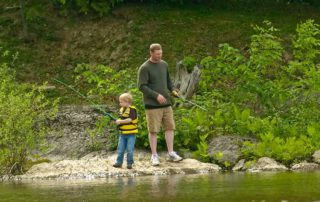 father and son fishing with poles on the shore of the lake