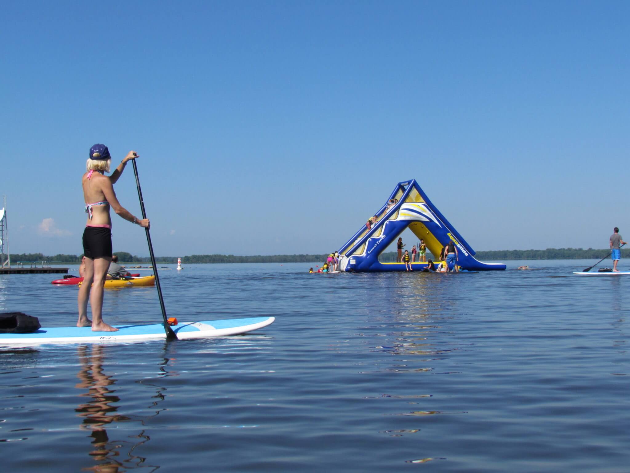 Woman standing on paddle board in the lake. Inflatable water toys in background